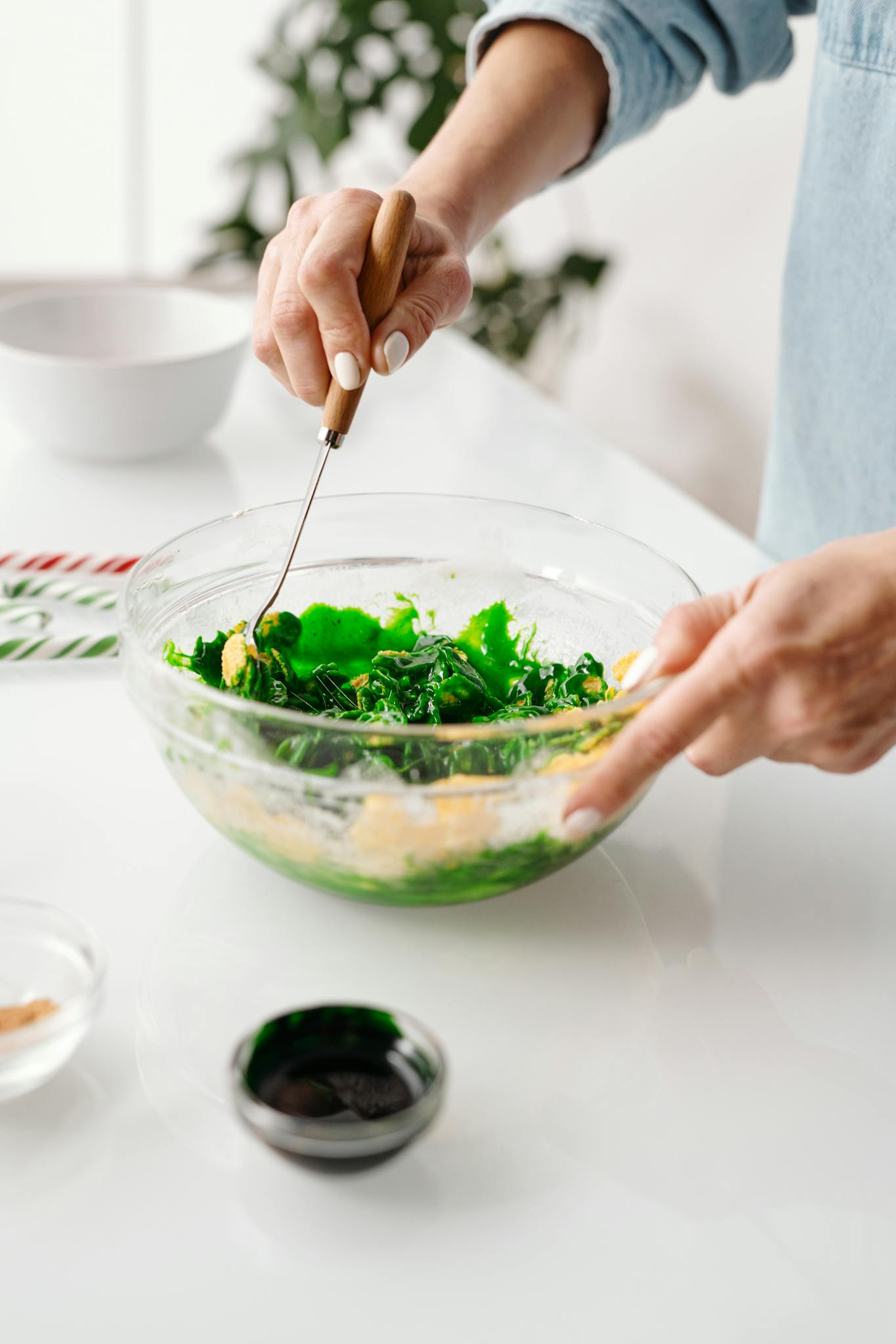 Close-up of hands mixing fresh green salad in a glass bowl in a bright kitchen.