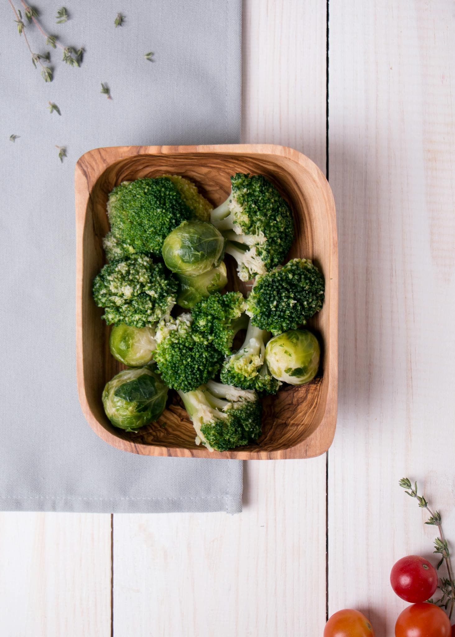 Fresh broccoli and Brussels sprouts in a wooden bowl on light wooden surface.