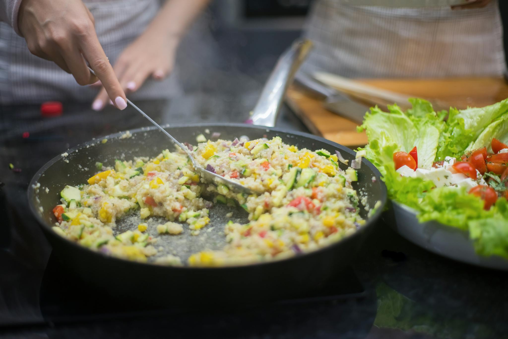 Fresh vegetable stir-fry in a pan with lettuce salad, captured in a kitchen setting.