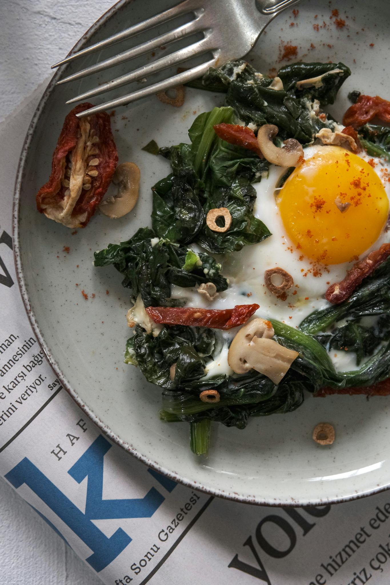 Top view of a nutritious dish with spinach, egg, and mushrooms on a earth-toned plate.